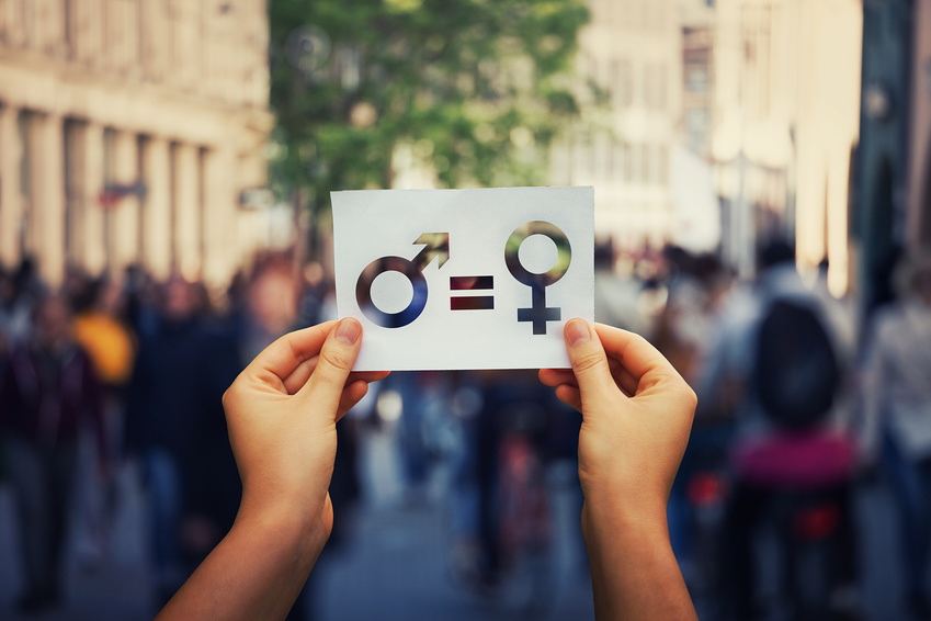 gender equality / ©1STunningART - stock.adobe.com, 1STunningART - stock.adobe.com Gender equality concept as woman hands holding a white paper sheet with male and female symbol over a crowded city street background. Sex sign as a metaphor of social issue.