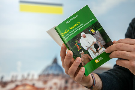Eine Person hält das Nachsynodale Apostolische Schreiben 'Querida Amazonia' von Papst Franziskus zur Amazonas-Synode in der Sprache Italienisch am 12. Februar 2020 auf einem Tisch im Vatikan. Im Hintergrund: ein Bild vom Petersdom.