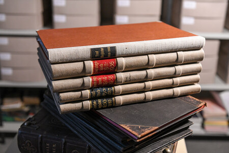 Auf einem Tisch im Archiv einer Kirchengemeinde liegen ein historisches Sterberegister, Taufbuch, Trauungsbuch und Taufregister. Hinter den Büchern steht ein Regal mit Archivboxen. (Aufnahmeort unbekannt)