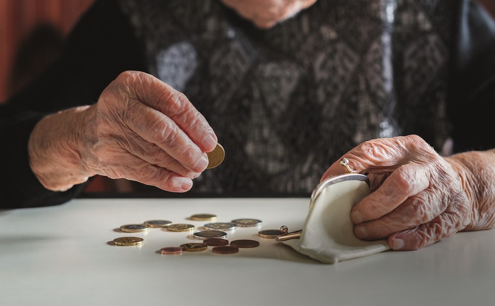 Elderly woman sitting at the table counting money in her wallet. / Matej Kastelic, kasto80 Elderly 95 years old woman sitting miserably at the table at home and counting remaining coins from the pension in her wallet after paying the bills.