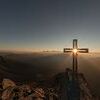 Kreuz auf einem Berggipfel im Gegenlicht