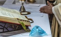 Ein Priester faltet die Hände und feiert den Gottesdienst am Altar, auf dem das Messbuch aufgeschlagen liegt, daneben eine einfache Atemschutzmaske, dahinter liturgische Geräte, am 8. Mai 2020 in Rom.
