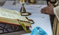 Ein Priester faltet die Hände und feiert den Gottesdienst am Altar, auf dem das Messbuch aufgeschlagen liegt, daneben eine einfache Atemschutzmaske, dahinter liturgische Geräte, am 8. Mai 2020 in Rom.