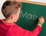 Ein Kind schreibt das Wort ' Mama ' auf eine Schultafel