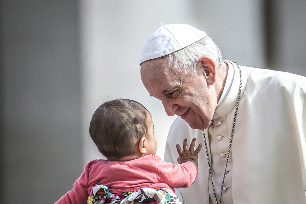 Papst Franziskus und Kleinkind / Copyright 2018, KNA (www.kna.de). Alle Rechte vorbehalten, Stefano Dal Pozzolo Ein Baby streckt seine Hand nach Papst Franziskus aus am 6. Juni 2018 im Vatikan. Der Papst schaut das Kind an und lächelt.